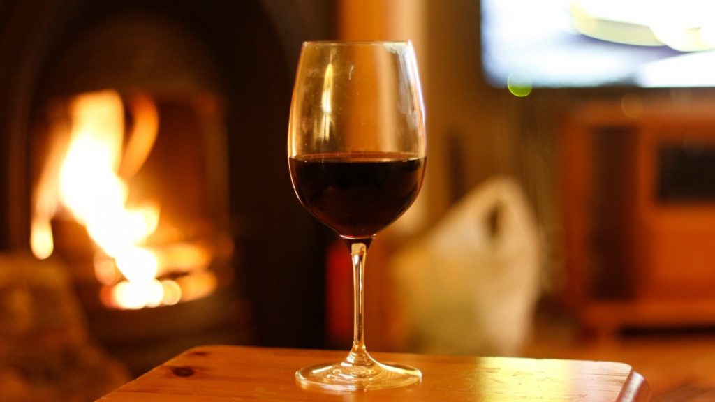 Third full glass of red wine on a high table near a fireplace