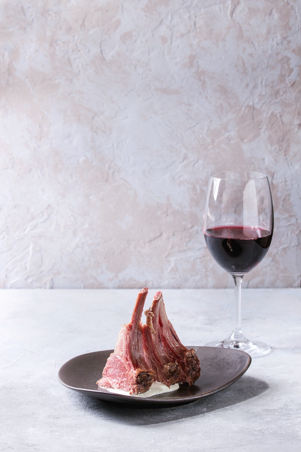 Grilled sliced lamb bar in a ceramic plate with a glass of red wine on a gray table