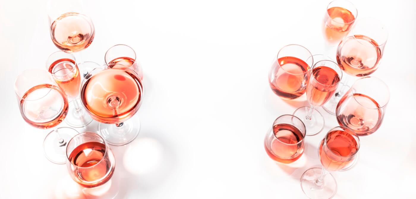 Several sizes of glasses of rosé wine on a white background