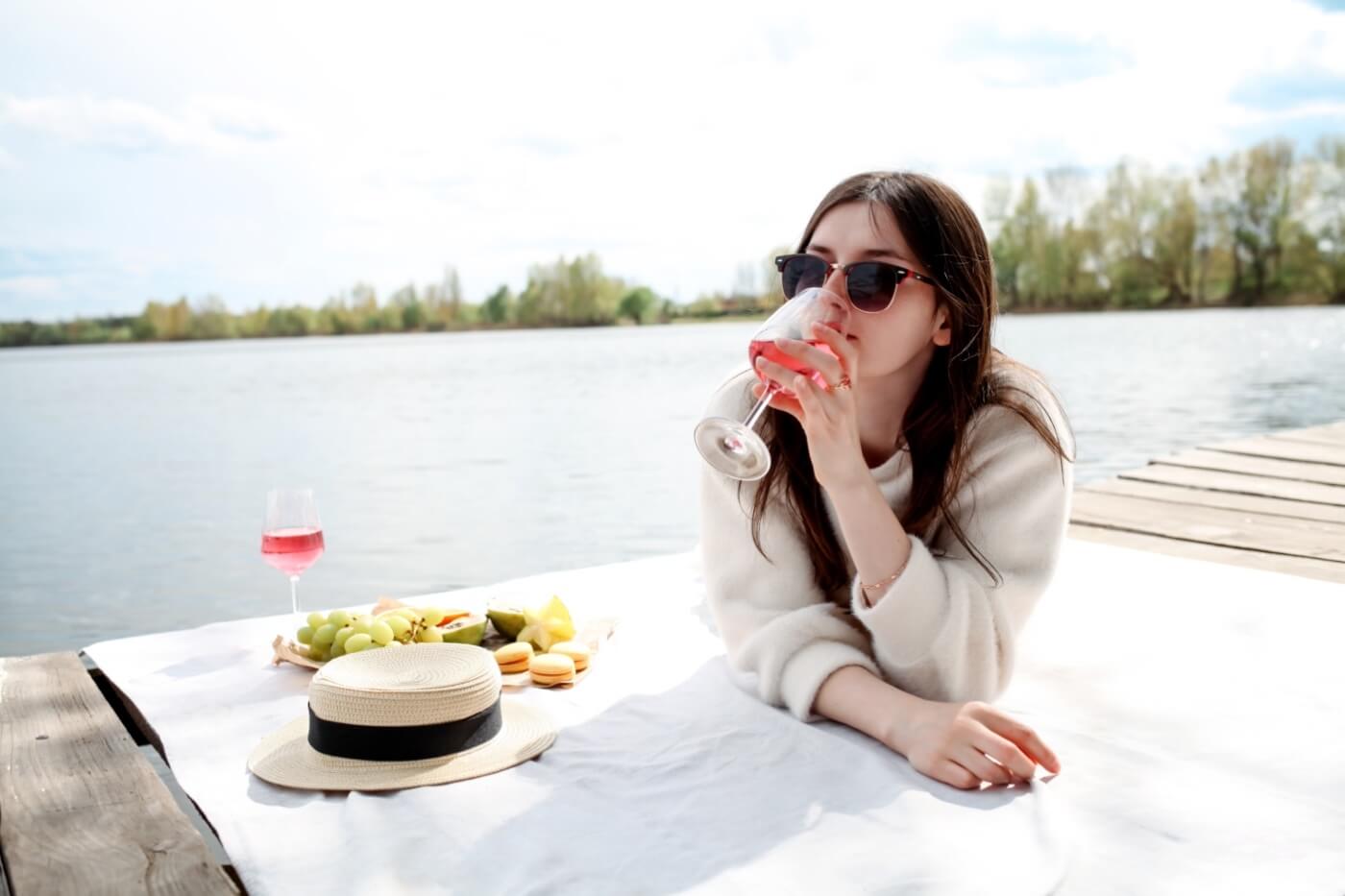 Femme buvant du vin rosé en pique-nique au bord d'un lac