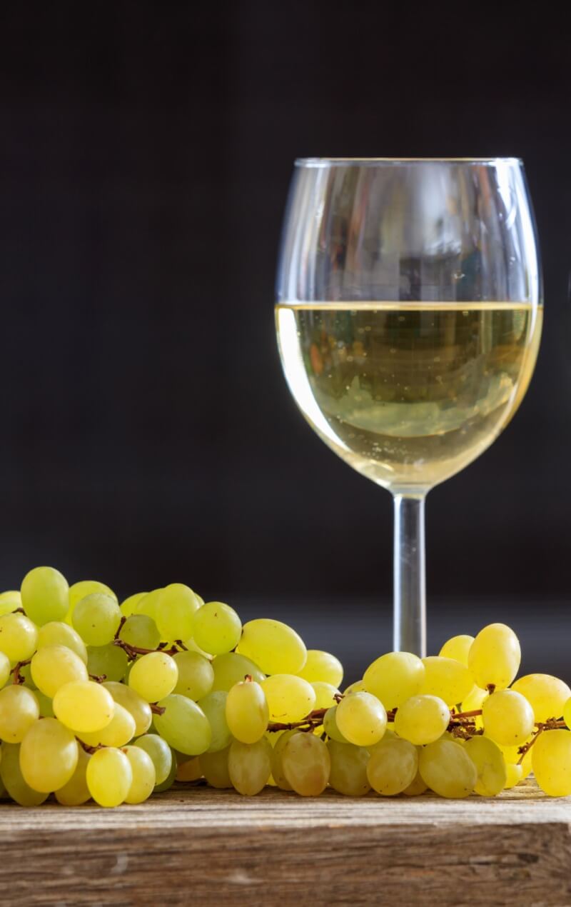 glass of white wine with grapes on a wooden table