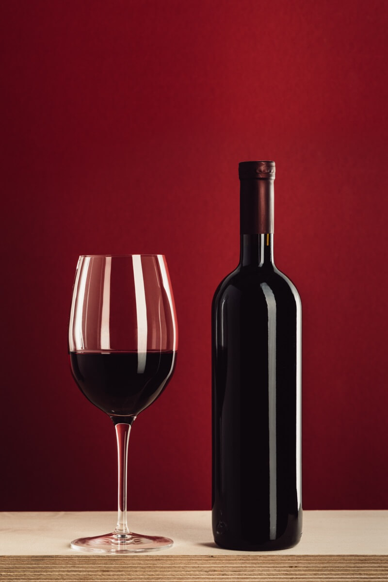 glass of wine to the left of a bottle of red wine on a wooden table