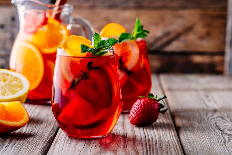 2 glasses of sangria accompanied by cut fruits including oranges and strawberries