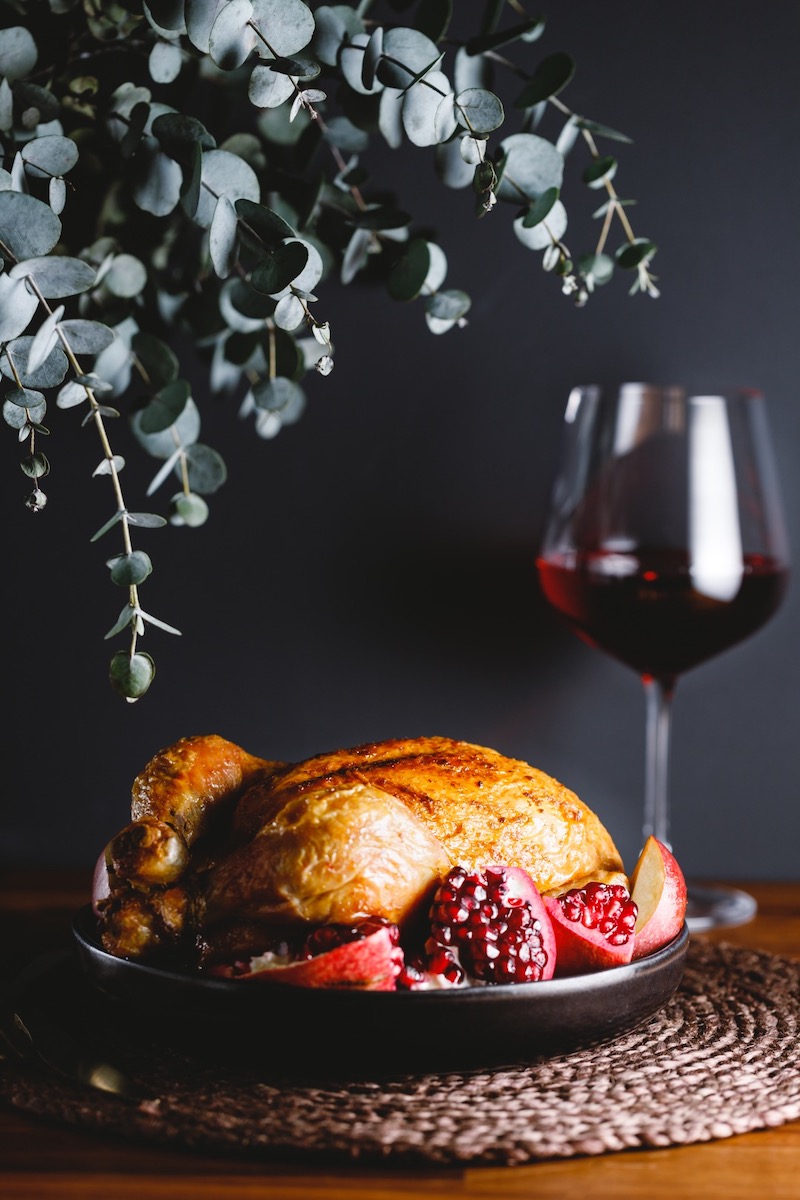 Une dinde rôtie avec grenade, pomme et vin rouge sur une table de fête.