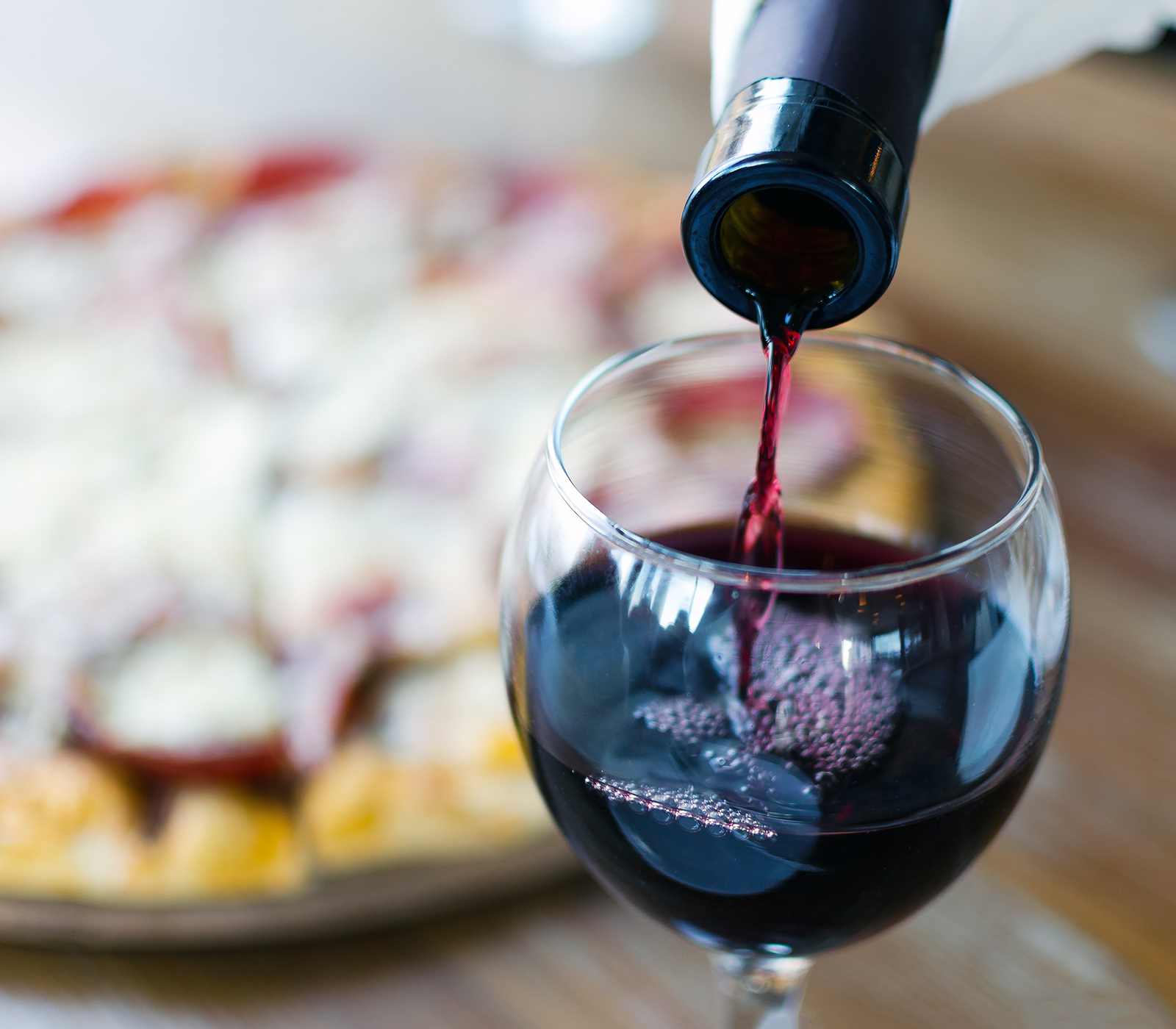 Filling a glass of red wine with a pizza